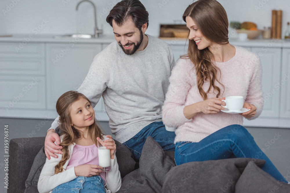 parents and daughter with milk and coffee on sofa