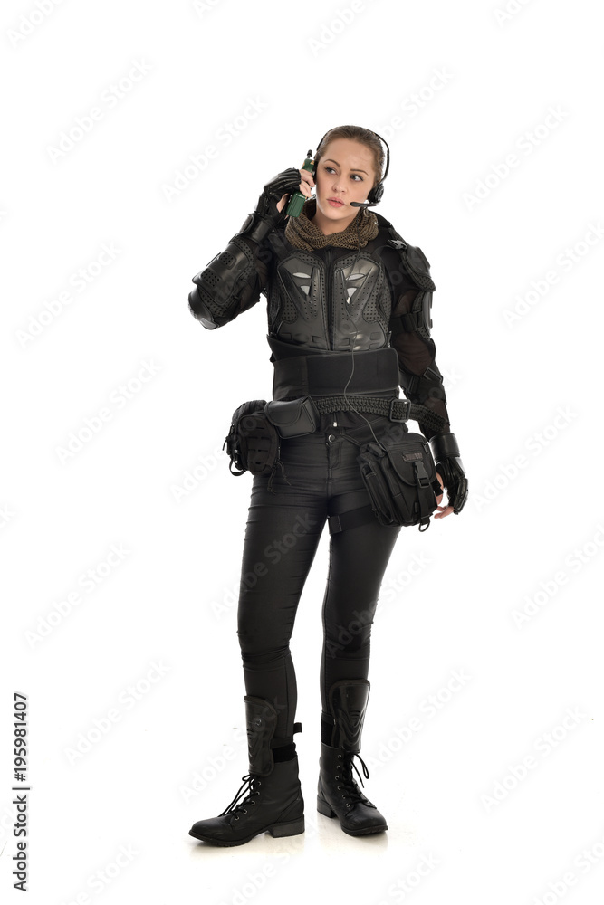 full length portrait of female  soldier wearing black  tactical armour, standing pose holding a walkie talkie, isolated on white studio background.