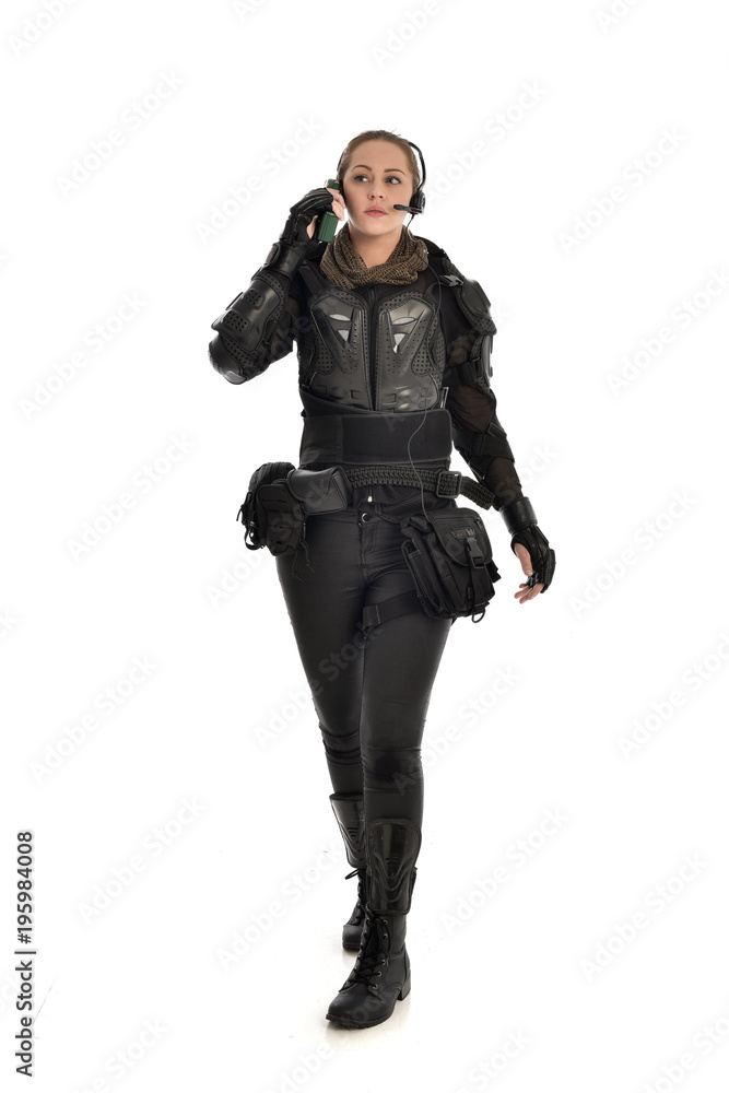 full length portrait of female soldier wearing black tactical armour, standing pose holding a walkie talkie, isolated on white studio background. full length portrait of female soldier wearing black tactical armour, standing pose holding a walkie talkie, isolated on white studio background.