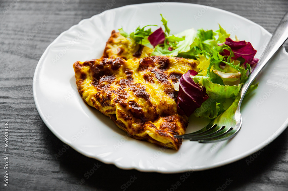 omelet with fresh mixed salad leaves in a plate on dark wooden background