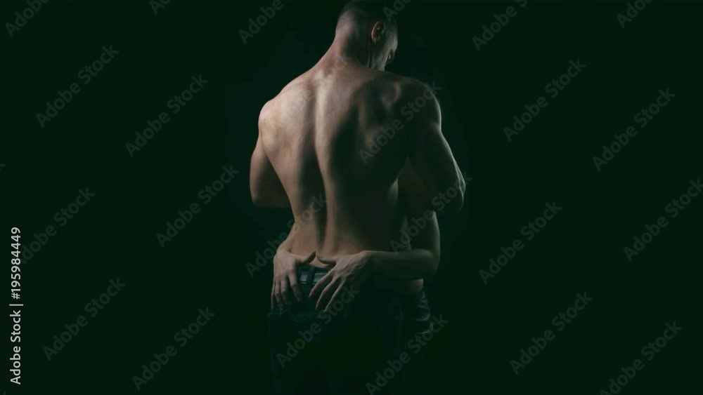Blond woman slowly touching back of young muscular shirtless man on black background. Blond woman slowly touching back of young muscular shirtless man on black background.