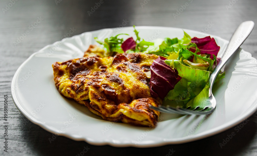 omelet with fresh mixed salad leaves in a plate on dark wooden background