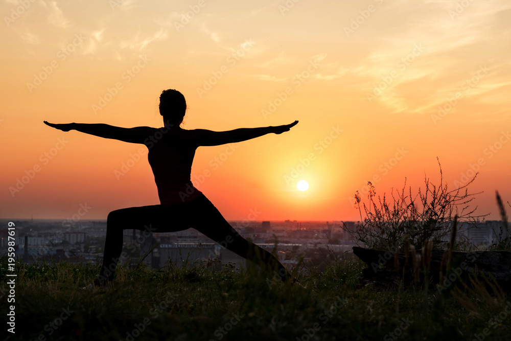 A woman does yoga in nature. Silhouette in sunset. Virabhadrasana - warrior pose