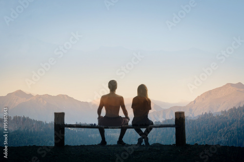 couple - a man and a woman sitting on a bench back to the camera and looking at the mountains. multiple exposure. sunse