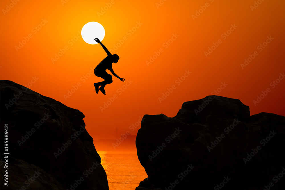 Man jumping over precipice between two rocky mountains at sunrise. Freedom, risk, challenge, success.