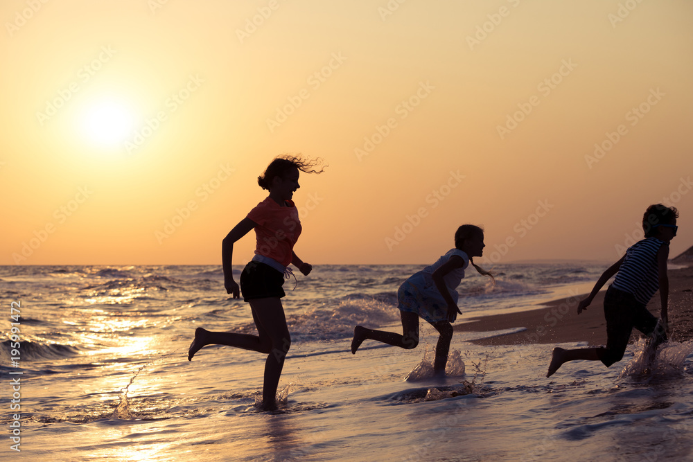 Happy children playing on the beach at the sunset time.