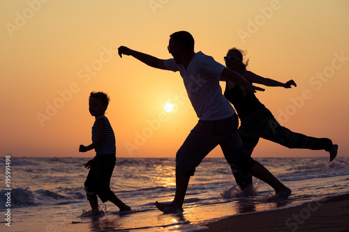 Father mother and son playing on the beach at the sunset time.
