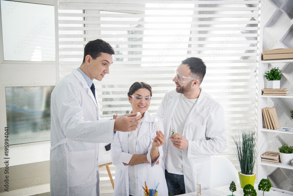 Happy with results. Delighted professional experienced scientists smiling and wearing uniforms and holding test tubes