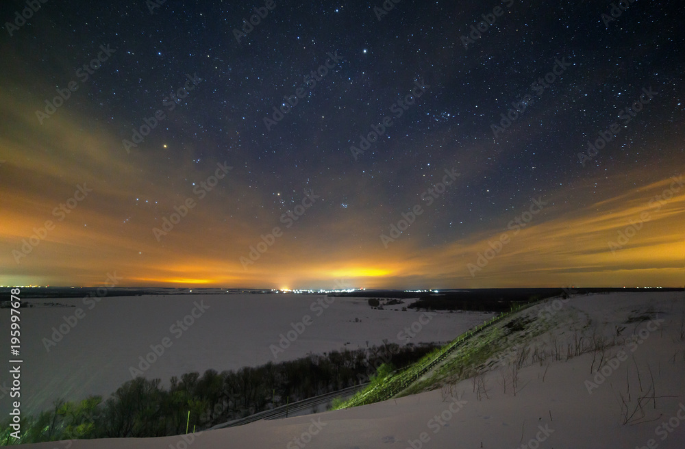 Stars of the night sky are hidden by clouds. Snowy winter landscape at dusk. City in the valley.