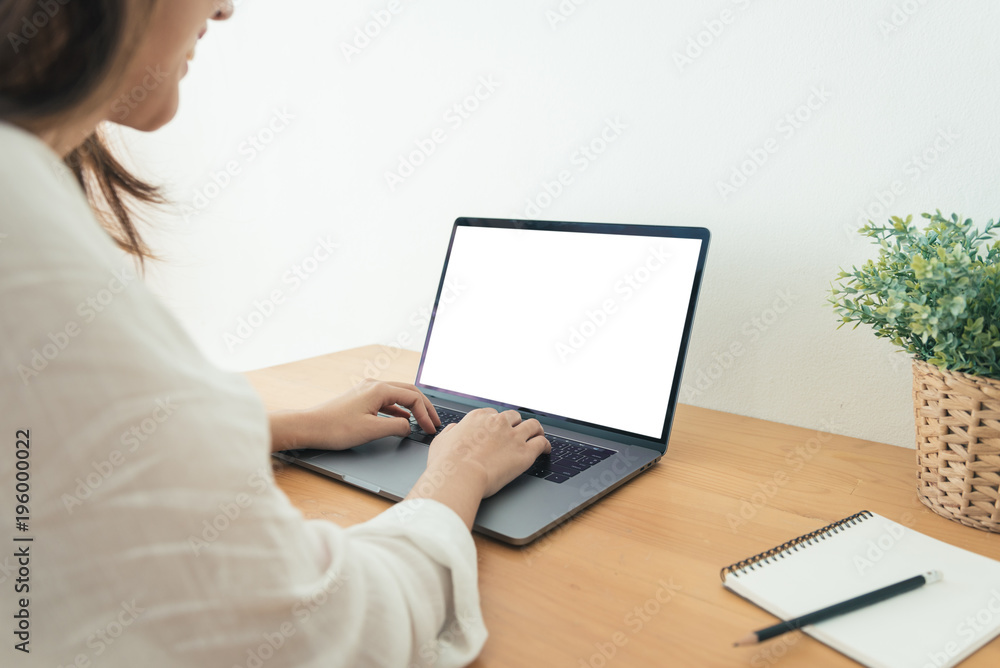 Fototapeta premium Young Asian woman working using and typing on laptop with mock up blank white screen while at home in office work space. Businesswoman working from home via portable computer. Enjoying time at home.