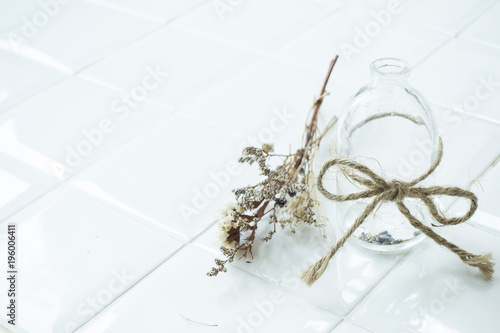 Empty transparent vintage bottle with rope and dried flower on white dining table