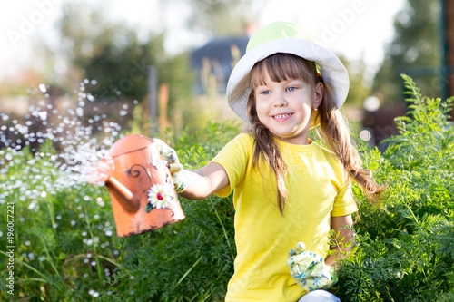 Little girl watering plants with can in a garden