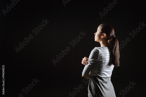 Loneliest and calm. Thoughtful cute fashionable lady standing in the empty room hugging herself and looking aside.