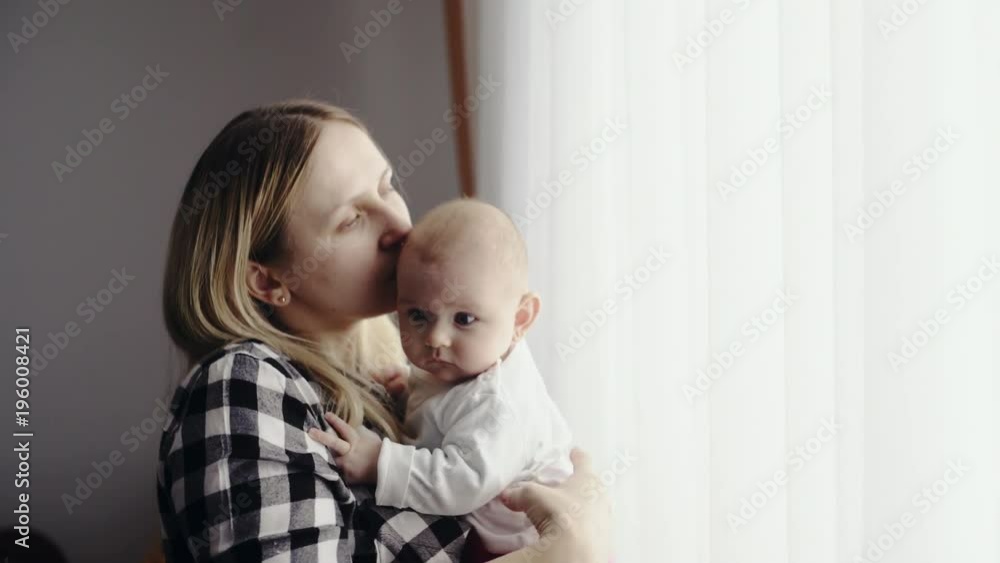 Happy mother with a newborn baby near a bright window in the bedroom Happy mother with a newborn baby near a bright window in the bedroom