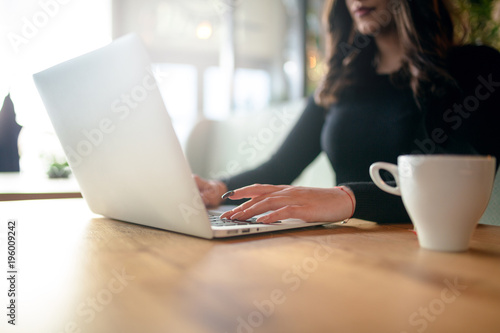 Cropped shot view of a women's hands keyboarding on laptop, young female person working on net-book while sitting in coffee shop indoors, brunette female freelancer connecting to internet via computer