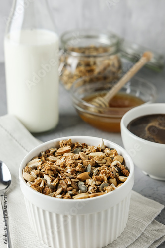 Homemade granola in a blue bowl on a linen napkin with a bottle of milk, cup of coffee and honey. Food Photography of a healthy morning breakfast.