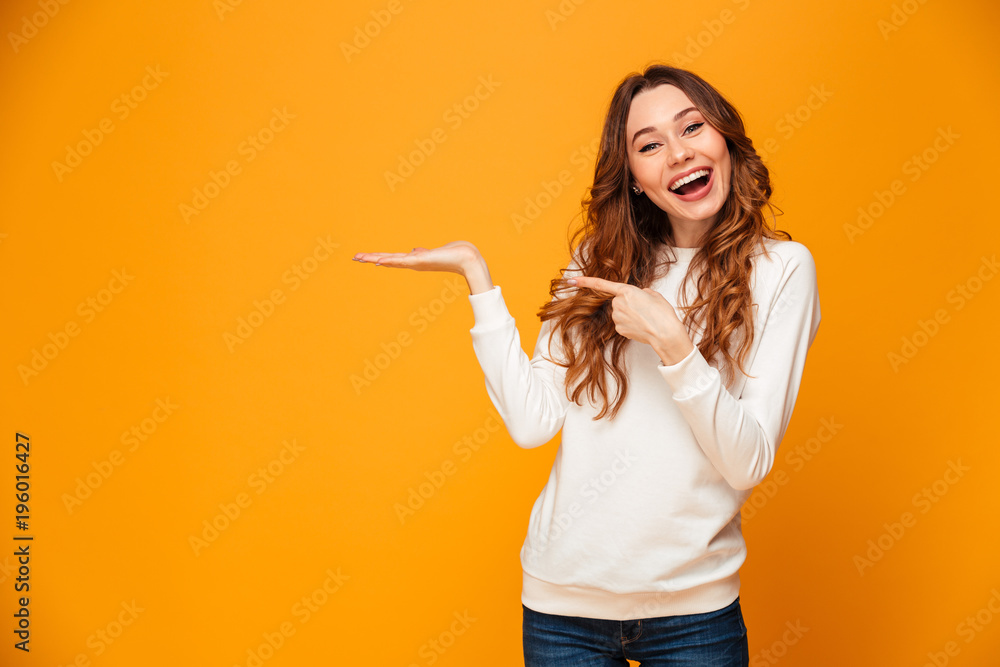 Pleased brunette woman in sweater holding copyspace on the palm - obrazy, fototapety, plakaty 