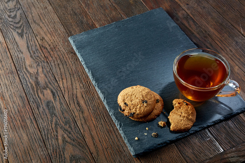Cup of tea with a couple of cookies on black board over a wooden background, top view, selective focus
