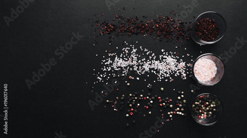 Glasses with flavored salt, assorted peppercorns and red spice on black background