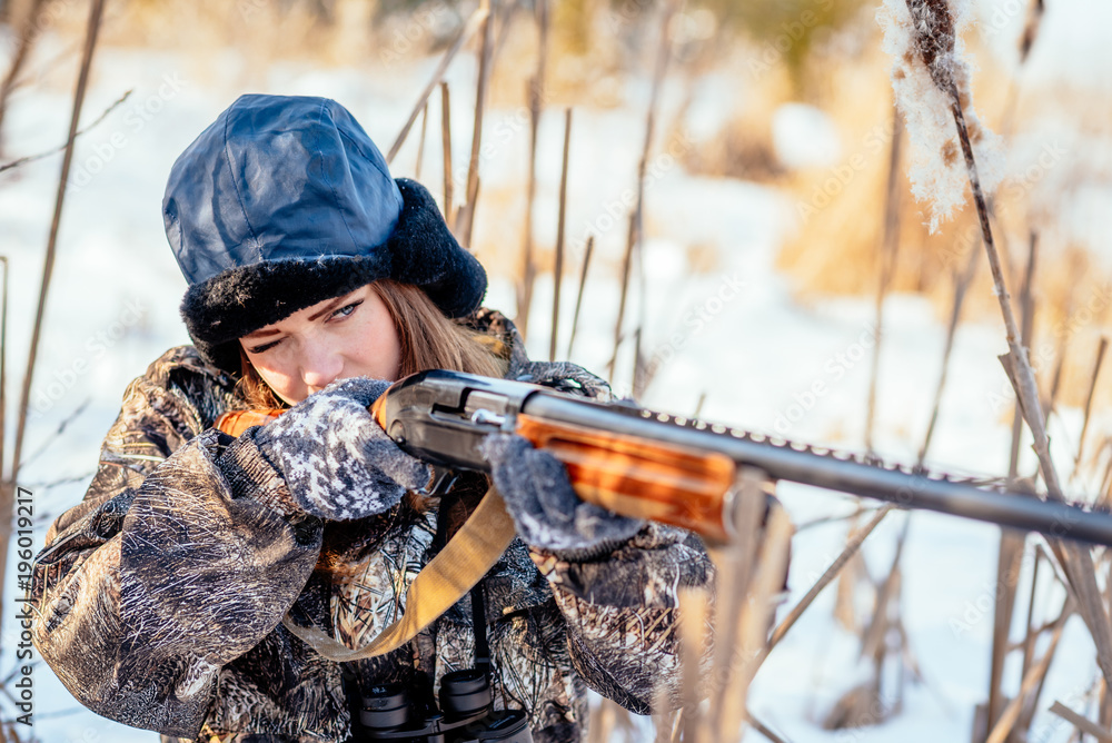 Fototapeta premium female hunter in camouflage clothes ready to hunt, holding gun and walking in forest. hunting and people concept