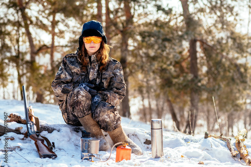 Female hunter preparing food with a portable gas burner in a winter forest. Bushcraft, hunting and people concept