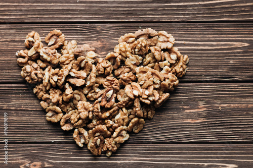 Heart shaped pile of shelled walnuts on wooden background, healthy eating concept