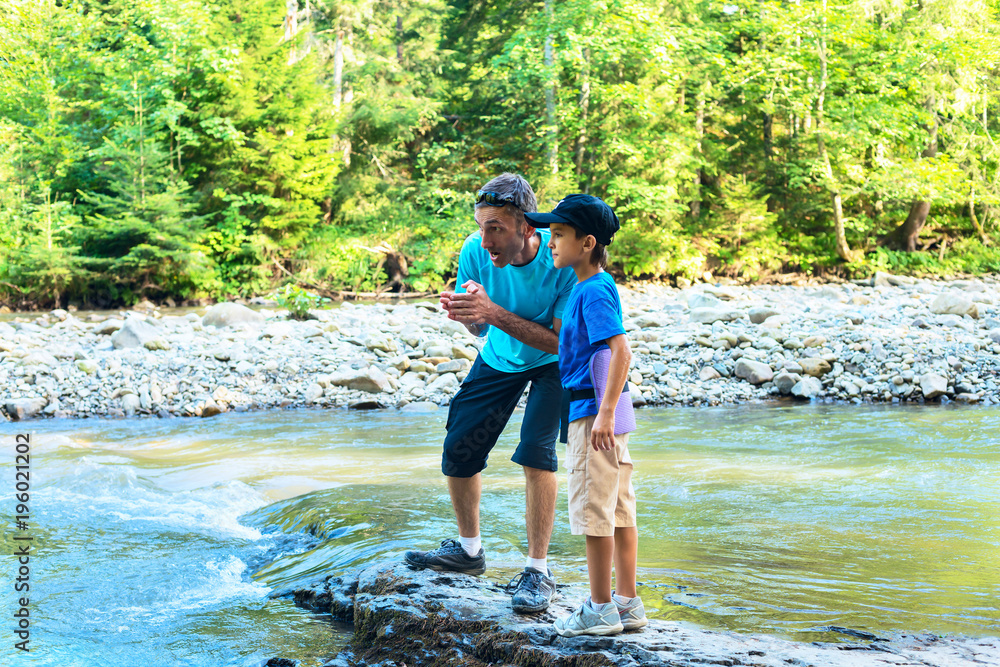 Travelers - father and son are standing on the shore of mountain river Travelers - father and son are standing on the shore of mountain river