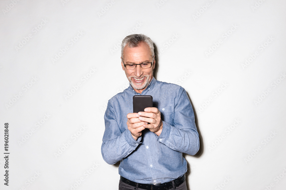 Happy old man in blue shirt using smartphone isolated Happy old man in blue shirt using smartphone isolated