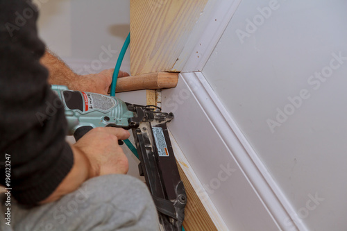 Carpenter brad using nail gun to Moulding trim, with the warning label that all power tools