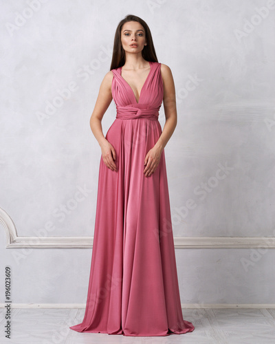 Canvas Print Beautiful long haired young woman dressed in stylish red bandeau maxi dress posing against white wall on background