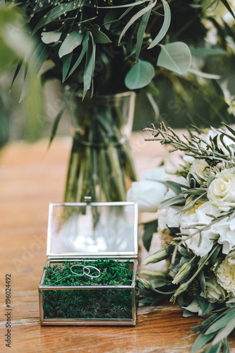 A beautiful glass jewerly box for wedding gold rings with moss. Near a bouquet of a bride with white flowers and eucalyptus on a wooden background photo