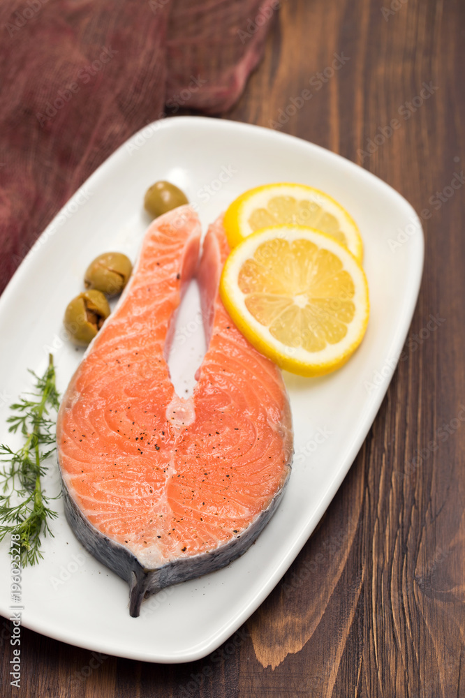 raw salmon with lemon on white dish on brown background
