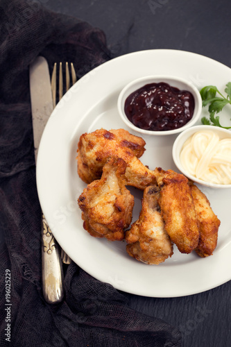 fried chicken with sauces on white plate on black background