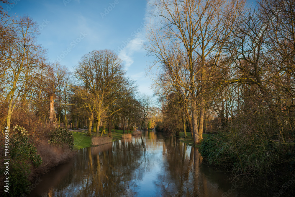 Beautiful autumn landscape in the park. River and quay with a trees on the shore reflected in water. Sun rays falling on the trees in warm sunny day Beautiful autumn landscape in the park. River and quay with a trees on the shore reflected in water. Sun rays falling on the trees in warm sunny day