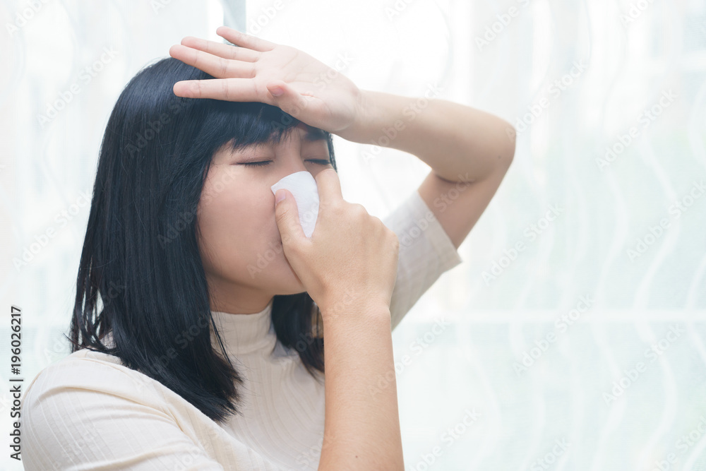 Woman with allergy or cold sneezing into napkin in her room - health concept.