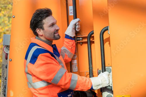 Принти на полотні Waste collector gripping handle of garbage truck riding on the platform