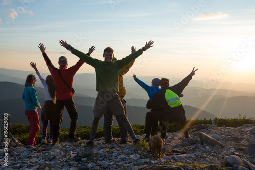 Happy hikers, friends with open arms are standing on a top