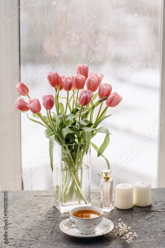 a Cup of tea, perfume, bouquet of tulips, candles, on a gray table by the window