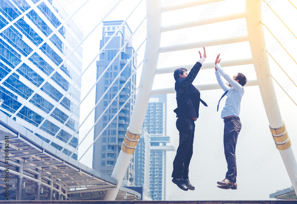 Happy successful two businessman jumping clap each other hand in the air. Two man happily jumping as a business achievement, achieve goal. Business conceptual. Happy successful two businessman jumping clap each other hand in the air. Two man happily jumping as a business achievement, achieve goal. Business conceptual.