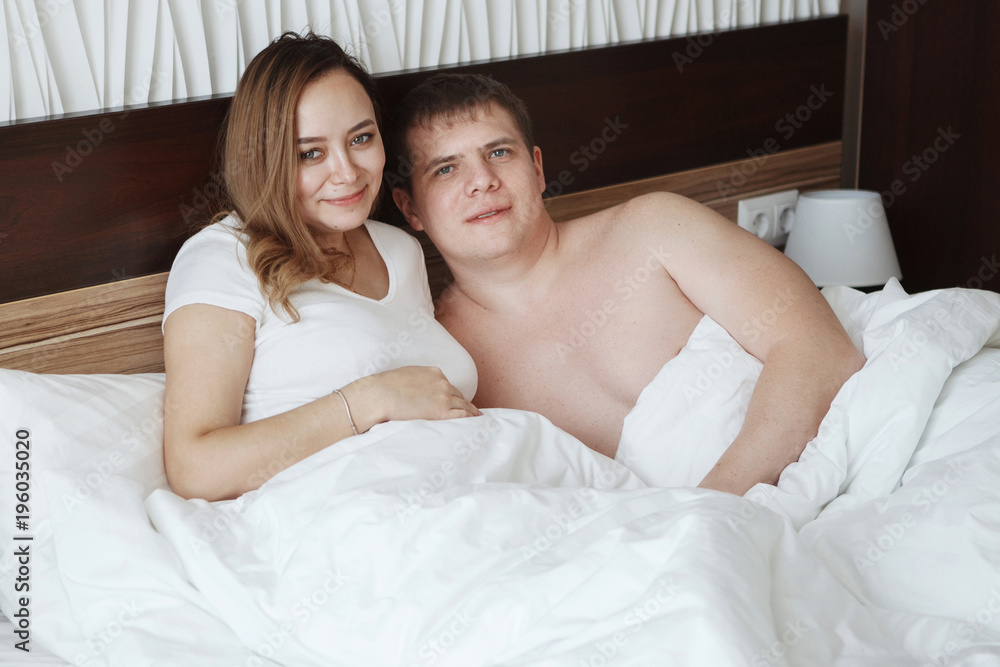 Young beautiful husband and wife resting in bed under a white blanket in a hotel room Young beautiful husband and wife resting in bed under a white blanket in a hotel room