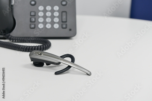 Wireless headset is on the white table with black IP or office phone at behind