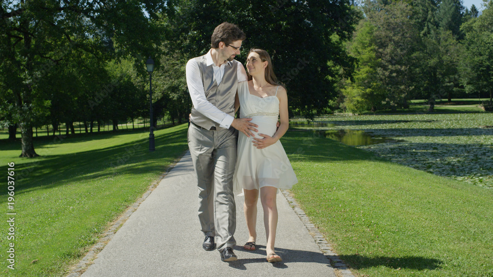 Fototapeta premium Happy young couple gaze at each other while gently stroking her pregnant belly