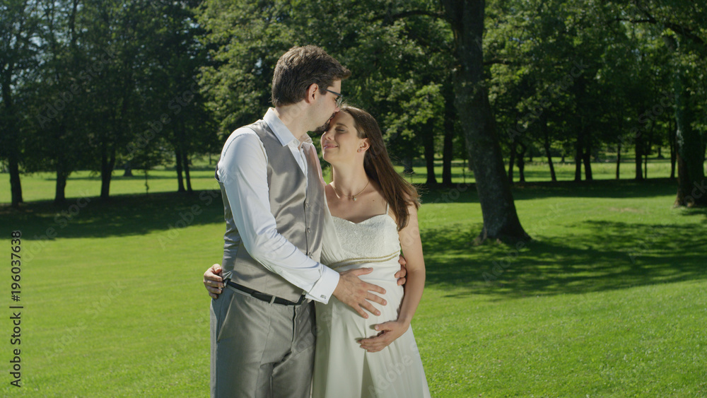 Caring husband kissing his beautiful pregnant wife on the forehead on sunny day Caring husband kissing his beautiful pregnant wife on the forehead on sunny day