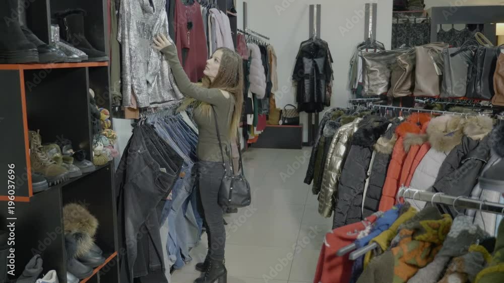 Attractive female model wearing heels browsing clothes to buy in a shopping store mall