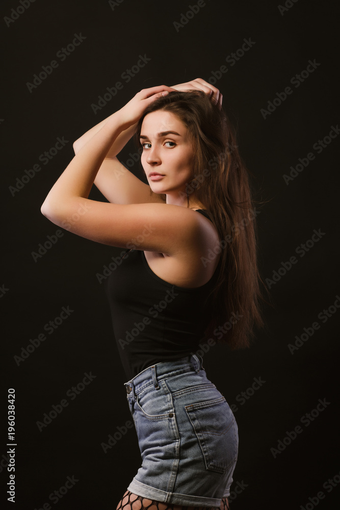 Model test with sexy young model in black shirt and jeans shorts posing in the shadows