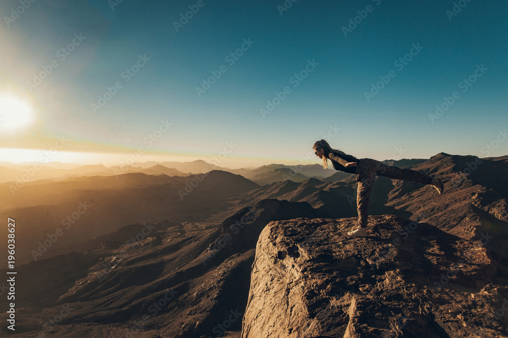 Woman does yoga exercises on edge of cliff on Mount Sinai against background of sunrise.