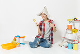 Fun woman in newspaper hat sitting on floor with brush, instruments for renovation apartment room isolated on white background. Wallpaper, accessories for gluing, painting tools. Repair home concept.