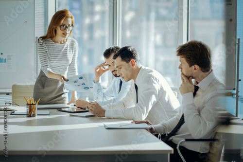 Unsatisfied with performance. Pretty young female boss holding printouts with inaccurate research results and reprimanding her employees for a poor performance photo