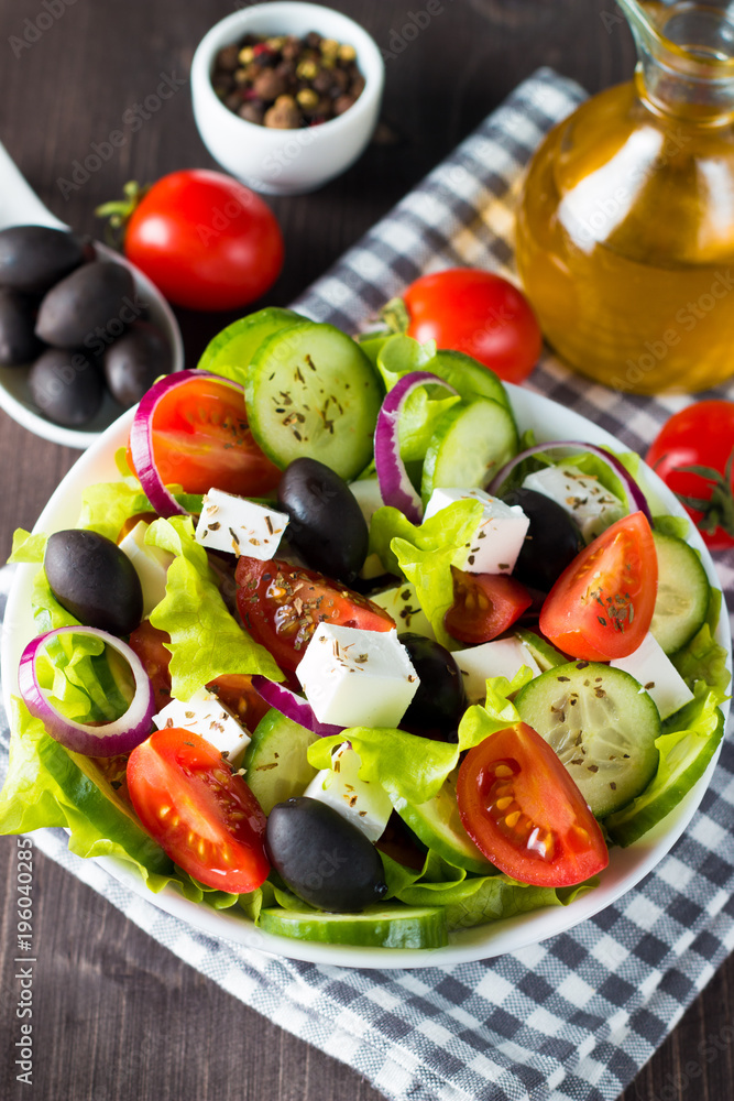 Fresh Greek salad made of cherry tomato, ruccola, arugula, feta, olives, cucumbers, onion and spices. Caesar salad in a white bowl on wooden background. Healthy organic diet food concept. Fresh Greek salad made of cherry tomato, ruccola, arugula, feta, olives, cucumbers, onion and spices. Caesar salad in a white bowl on wooden background. Healthy organic diet food concept.