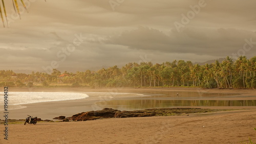 Lonely motorbike standing in the middle of peaceful exotic beach near rainforest